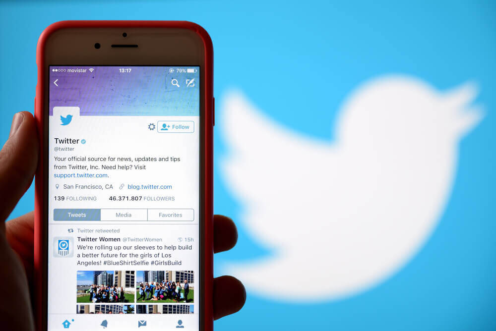 Phone showing the twitter app as the twitter logo is shown on the background