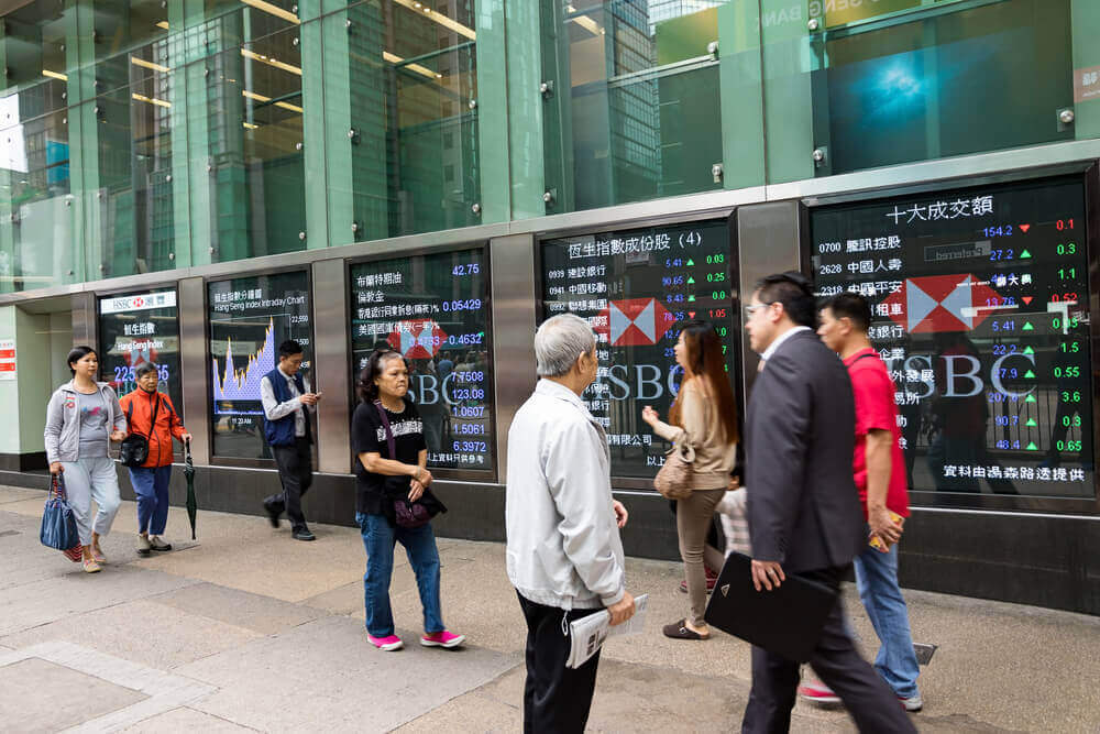 Asian shares are shown on electronic boards as people are walking by