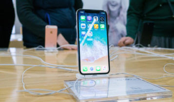 iphone x displayed on a clear stand on a table and two people in the background