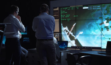 people analyzing with their computers and a screen that shows a spacecraft with numbers
