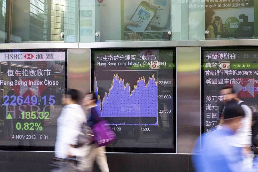 blurred effect of people walking by electronic boards showing the stock market quotes and charts