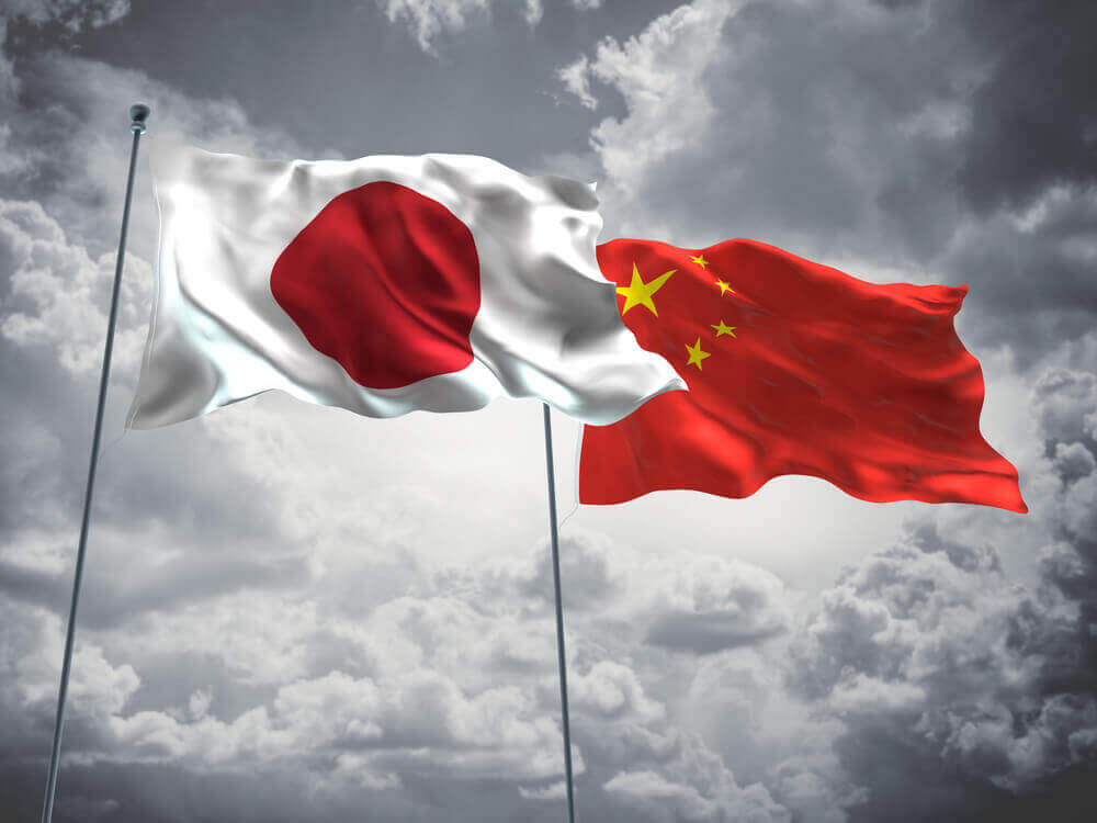 Japan and China flag on poles waving with a black and white clouds background