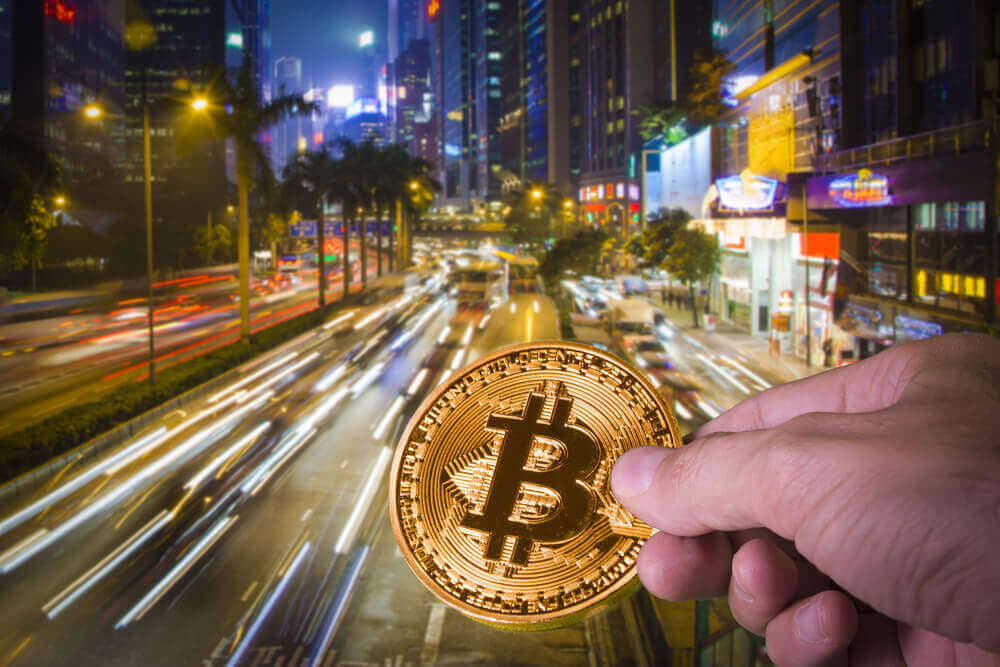 a blurred background of a street in hong kong and a bitcoin being held by a hand