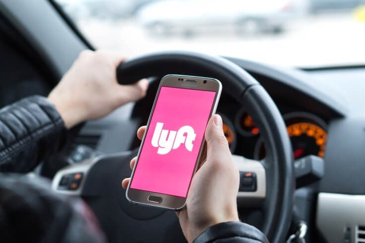Finance Brokerage-Public Offering: man in a car holding a phone with Lyft logo on screen
