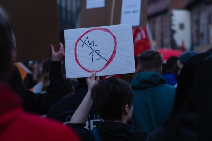 Finance Brokerage-Copyrights: protester holding placard with “Art. 13” written and crossed out 