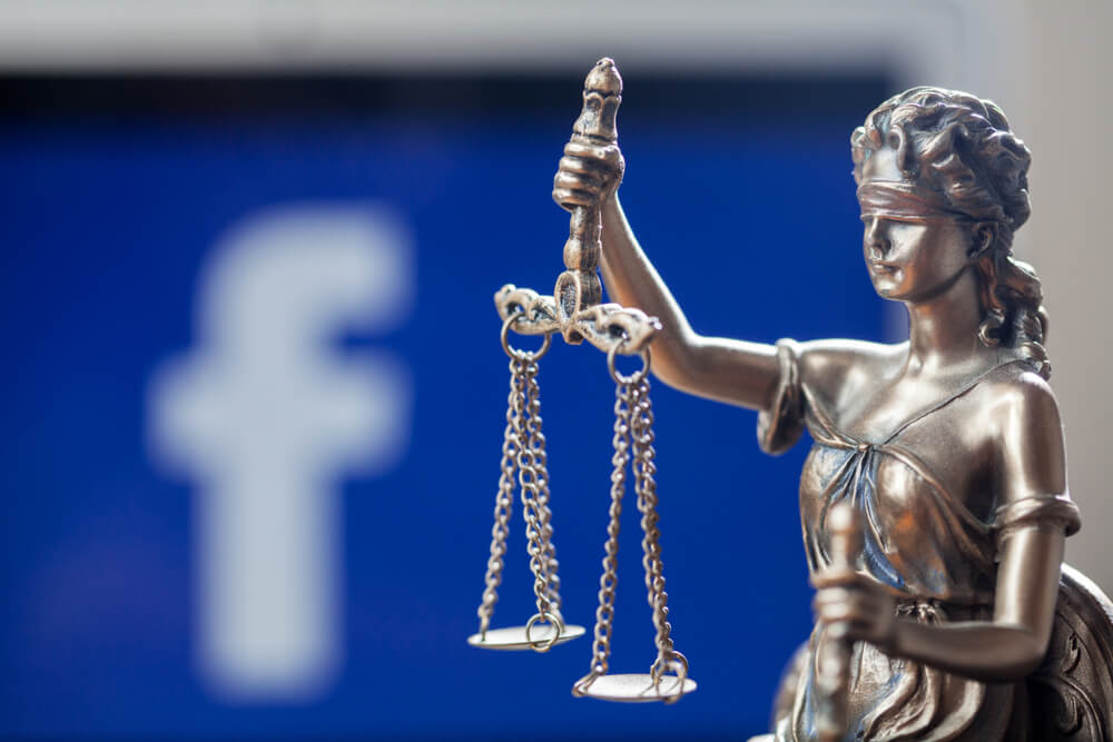 Blind folded Lady Justice Statue in front of a laptop with social network Facebook logo on the screen.