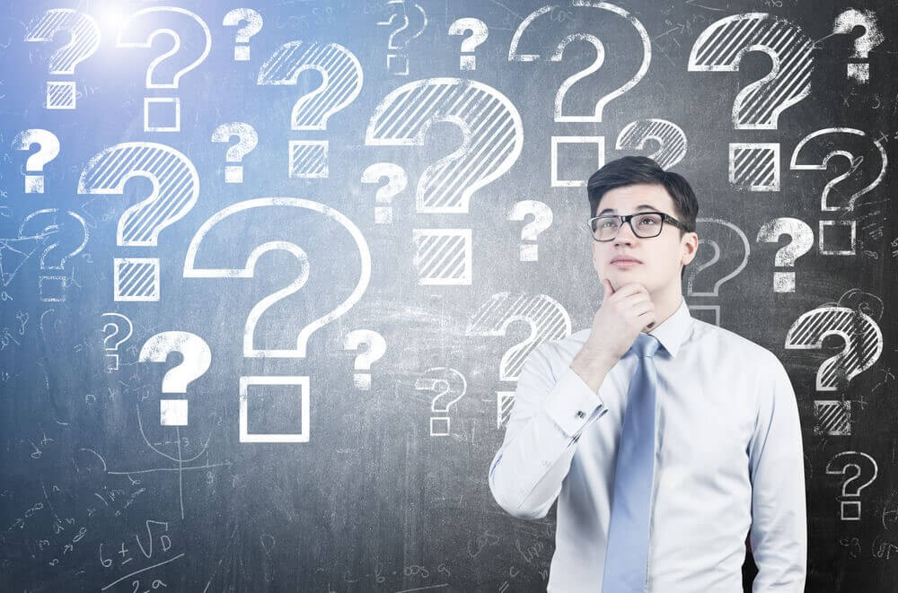 A man thinking in front of a wall of question marks.