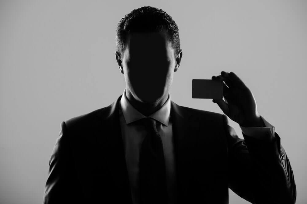 Broker: Faceless man in formal suit and tie on grey background.