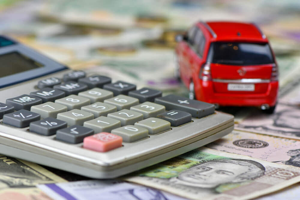Calculator and red toy car on a variety of national currency banknotes background.