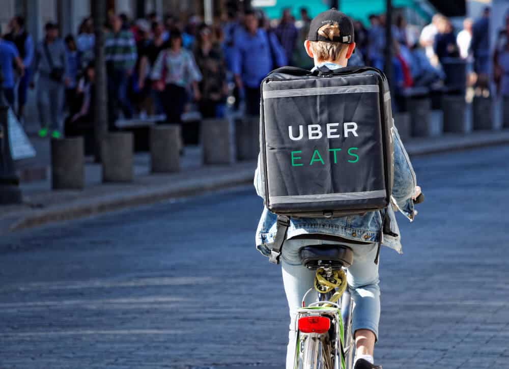 Food supplier with Uber Eats backpack riding a bike on the street.