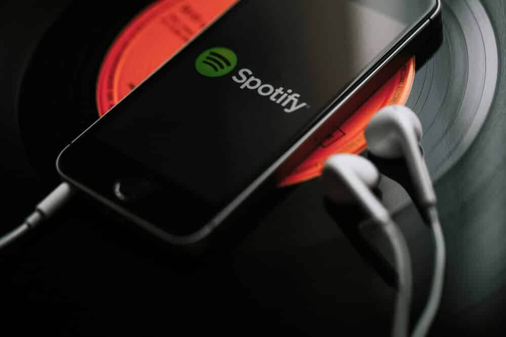 Mobile phone with Spotify Music service on the screen and white earphones on a black vinyl record.