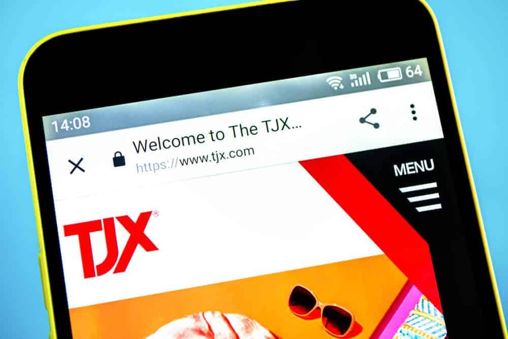 TJX Cos website homepage. TJX Cos logo visible on the phone screen.