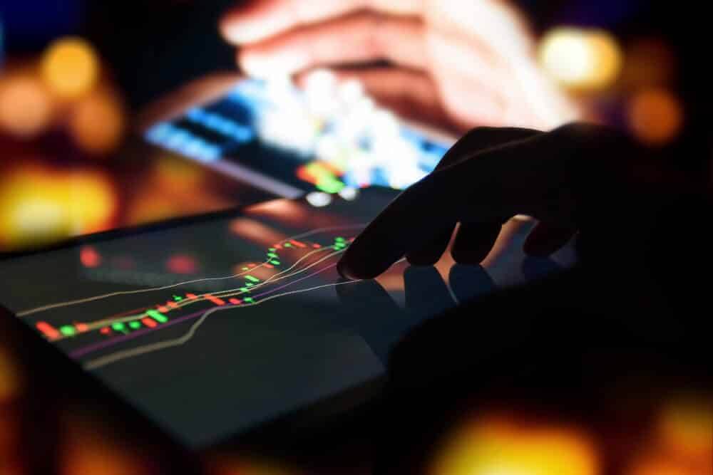 Silhouette finger on tablet with graph stock market trading screen.