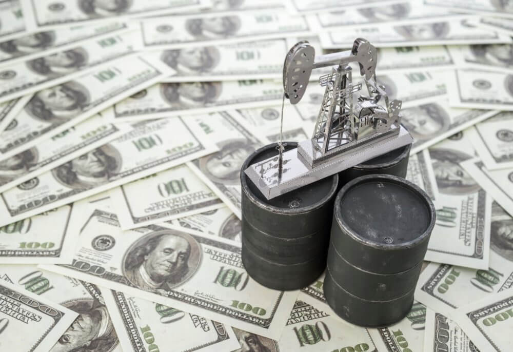 Três barris de petróleo embaixo de notas de dólar