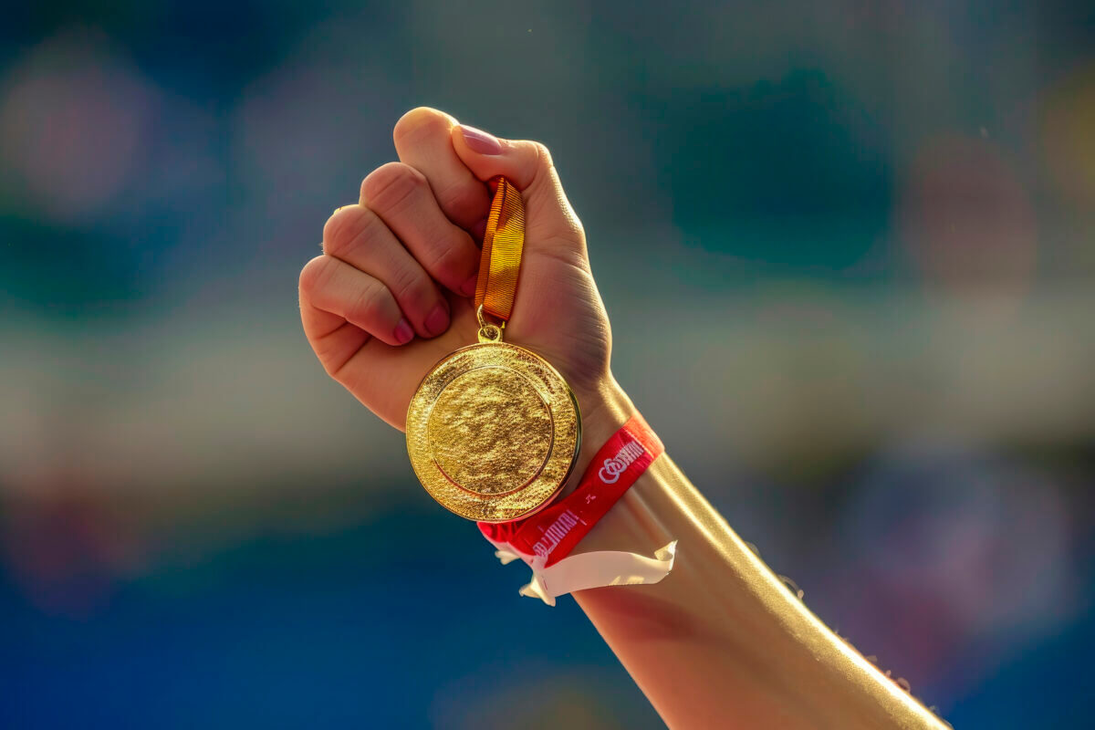 Mano de una mujer levantando una medalla de oro olímpica en señal de victoria